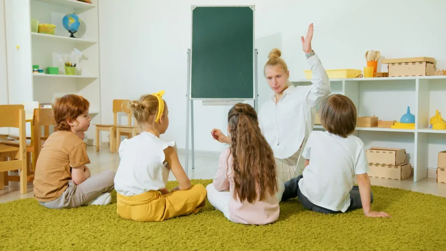 Une éducatrice échange avec quatre jeunes enfants assis sur un tapis dans un milieu éducatif lumineux.